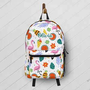 May include: White backpack with a colorful pattern of pink flamingos, watermelons, pineapples, ice cream cones, and flowers. The name "Olivia" is printed on the front. The backpack has a black zipper and straps, and a side mesh pocket.