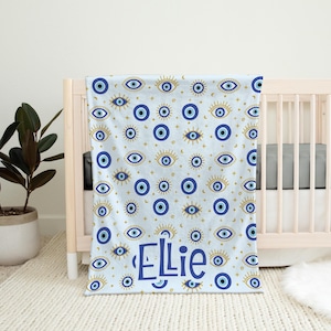 May include: A blue and gold baby blanket with a pattern of evil eyes and the name "Ellie" printed on it.