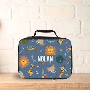 May include: A blue lunch bag with a zipper closure and a black handle. The bag has a pattern of animals, including lions, giraffes, and elephants, and the text "NOLAN" is printed on the front.