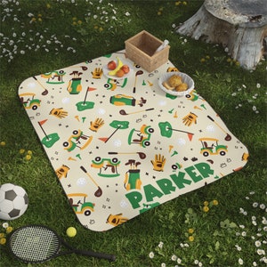 Könnte beinhalten: Eine beige Picknickdecke mit einem grün-gelben Golf-Motiv. Die Decke zeigt Golfwagen, Golfschläger, Golfbälle und Handschuhe. Der Text "Parker" ist in grünen Buchstaben auf der Decke gedruckt.