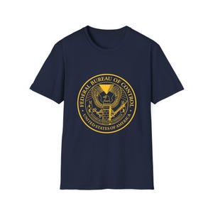 May include: A navy blue t-shirt with a yellow graphic of the Federal Bureau of Control seal. The seal features an eagle with a pyramid and the words "Federal Bureau of Control" and "United States of America".
