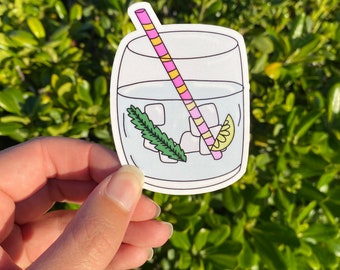 Könnte beinhalten: Ein Aufkleber mit einem Glas Limonade mit einem rosa-gelb gestreiften Strohhalm, Eiswürfeln, einer Zitronenscheibe und einem Minzblatt.