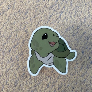 May include: A green cartoon turtle sticker with a shell and a smiling face.