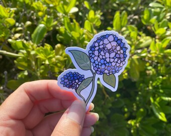 Puede incluir: Una pegatina de una flor de hortensia morada y azul con hojas verdes.