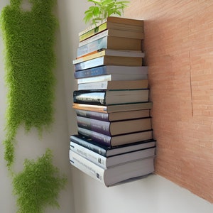 Op de afbeelding: Een stapel boeken in verschillende kleuren en maten, met enkele zichtbare titels, leunt tegen een muur. De boeken zijn in een verticale stapel gerangschikt, waarbij het bovenste boek het kleinste en het onderste boek het grootste is. De boeken zijn allemaal gebonden en hebben verschillende ontwerpen op hun omslagen.