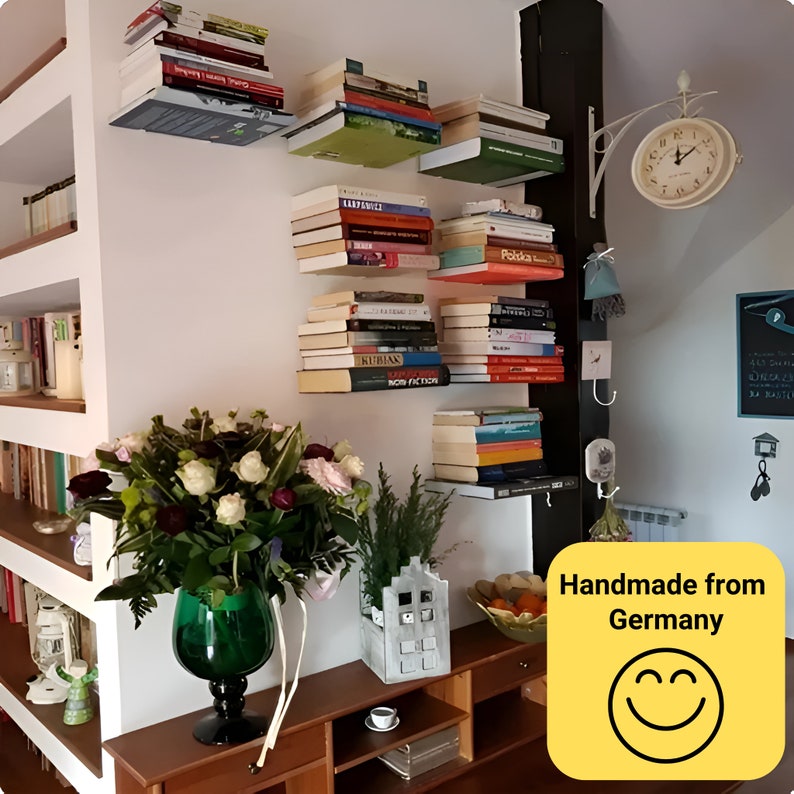 Peut inclure: Un mur blanc avec un ensemble d'&eacute;tag&egrave;res flottantes contenant des livres. Les &eacute;tag&egrave;res sont en bois et ont un cadre en m&eacute;tal noir. Les &eacute;tag&egrave;res sont fix&eacute;es au mur avec des vis. Il y a un bouquet de fleurs dans un vase vert sur une table en bois sous les &eacute;tag&egrave;res. Le texte "Handmade from Germany" est sur un carr&eacute; jaune avec un smiley.