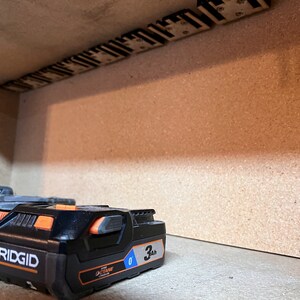 May include: Three black and orange Ridgid 3Ah batteries for a power tool. The batteries are on a brown surface.