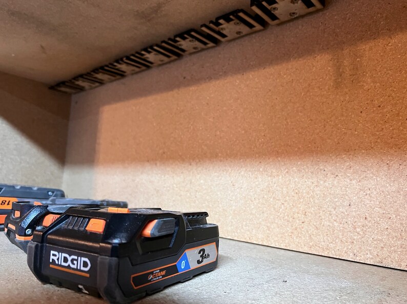 May include: Three black and orange Ridgid 3Ah batteries for a power tool. The batteries are on a brown surface.
