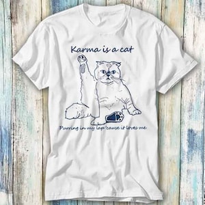May include: White t-shirt with a blue illustration of a cat with the text "Karma is a cat Purring in my lap 'cause it loves me".