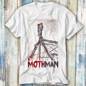 May include: White t-shirt with a graphic print of a creature with large wings perched on a metal structure. The text "Mothman" is printed in red below the image.