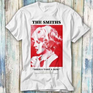 May include: White t-shirt with a red graphic of a woman's face and the text "THE SMITHS" and "SHEILA TAKE A BOW".