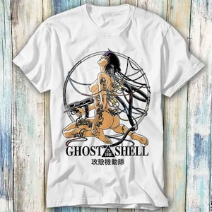 Könnte beinhalten: Weißes T-Shirt mit einer Illustration einer Cyborg-Frau mit einer Waffe, umgeben von Drähten, und dem Text "GHOST IN THE SHELL" in Schwarz. Japanischer Text befindet sich darunter. Das Design ist mittig auf dem Shirt platziert.