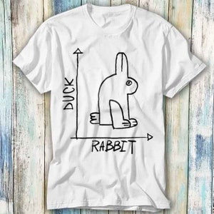Peut inclure: T-shirt blanc avec un dessin au trait noir d'un lapin avec les mots "Duck" et "Rabbit" sur un graphique.
