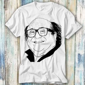 May include: A white t-shirt with a black and white line drawing of a man with glasses and a mustache. The man is smiling and has a round face.