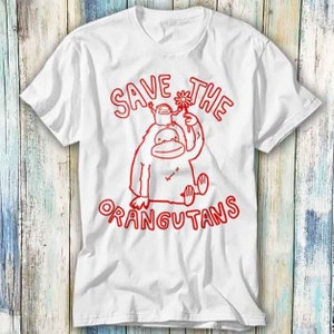 Puede incluir: Camiseta blanca con un gráfico rojo de un orangután sosteniendo una flor y un orangután más pequeño. El texto "Save the Orangutans" está escrito en rojo.