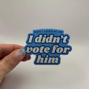 May include: A blue and white sticker with the text "Don't look at me I didn't vote for him" in a retro font.