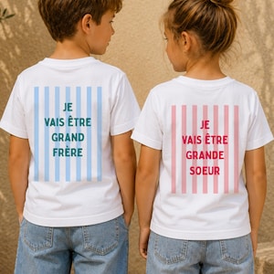 Op de afbeelding: Twee witte t-shirts van achteren gezien. Het linker t-shirt heeft lichtblauwe verticale strepen met de tekst JE VAIS ÊTRE GRAND FRÈRE. Het rechter t-shirt heeft lichtroze verticale strepen met de tekst JE VAIS ÊTRE GRANDE SOEUR.