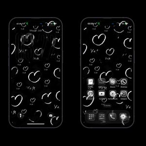 Könnte beinhalten: Zwei Smartphones mit schwarzem Hintergrund, einem weißen, handgezeichneten Herzmuster und dem Text V+M. Der linke Bildschirm zeigt den Sperrbildschirm mit einer großen Digitaluhr, der rechte den Startbildschirm mit App-Symbolen.