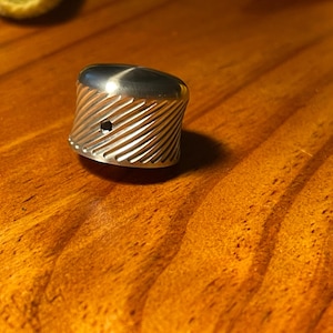 May include: A silver metal knob with a textured, grooved design. The knob has a small hole in the centre.