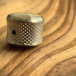 May include: A silver metal guitar knob with a diamond pattern. The knob has a small hole in the center.