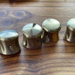 May include: Four gold-colored metal knobs with a textured surface. The knobs are round and have a small hole in the center.