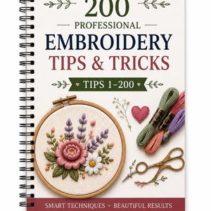 Peut inclure: Un livre à reliure spirale intitulé 200 PROFESSIONAL EMBROIDERY TIPS & TRICKS. La couverture présente un tambour à broder avec un motif floral, trois échevettes de fil en vert, rose et violet, un petit cœur et des ciseaux dorés.