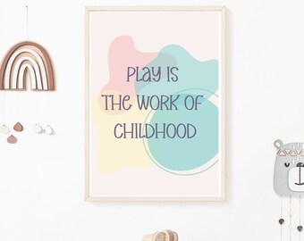 May include: A framed print with a light pink, yellow, and blue abstract design. The text "Play is the work of childhood" is written in purple on the print.