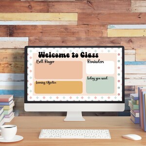 May include: A computer monitor displays a classroom welcome screen with the text "Welcome to Class." The screen includes sections for "Bell Ringer," "Reminders," "Learning Objective," and "Today you need." A keyboard, mouse, coffee cup, and books are on the desk.