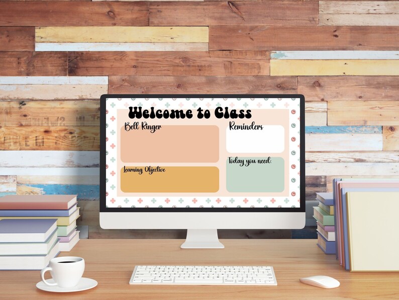 May include: A computer monitor displays a classroom welcome screen with the text "Welcome to Class." The screen includes sections for "Bell Ringer," "Reminders," "Learning Objective," and "Today you need." A keyboard, mouse, coffee cup, and books are on the desk.