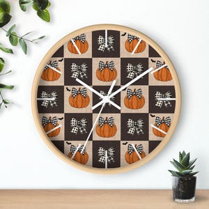 Puede incluir: Un reloj de pared redondo de madera con un patrón de cuadros que presenta calabazas naranjas y lazos negros y blancos. La esfera del reloj es blanca con manecillas negras.