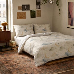 May include: A white duvet cover and two matching pillowcases featuring a repeating pattern of watercolor-style crescent moons, stars, and soft blue and green clouds. The bedding set is displayed on a bed with a white fitted sheet.