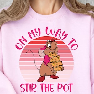 May include: Pink sweatshirt with a retro sunset graphic and a cartoon mouse holding a stack of cheese. The text on the sweatshirt reads "On my way to stir the pot."