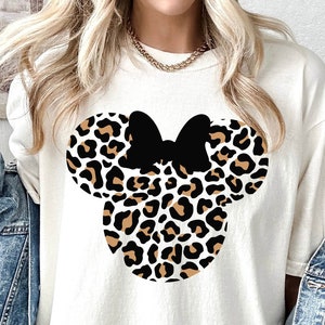 Peut inclure: Un t-shirt blanc avec un motif de t&ecirc;te de Minnie Mouse en imprim&eacute; l&eacute;opard noir et marron.