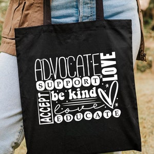 K&ouml;nnte beinhalten: Schwarze Tragetasche mit wei&szlig;em Text, der in einem kreisf&ouml;rmigen Design "Advocate, Support, Be Kind, Love, Educate" lautet.