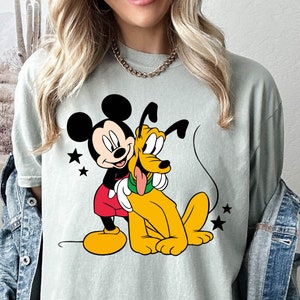 May include: A light green t-shirt with a cartoon image of Mickey Mouse and Pluto. Mickey Mouse is wearing red shorts and Pluto is wearing a green collar.