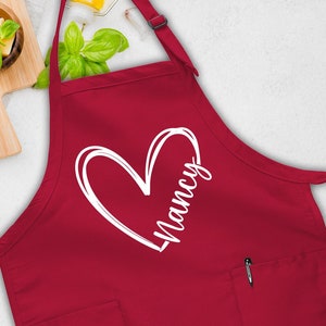 May include: Red kitchen apron with a white heart and the name "Nancy" printed on it.