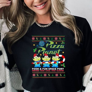 May include: Black t-shirt with a Christmas-themed design featuring the characters from the movie "Toy Story" and the text "Pizza Planet" and "Food & Fun Space Port".