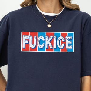 以下が含まれることがあります： 長方形のデザインで「FUCKICE」という言葉が入ったネイビーブルーのスウェットシャツ。テキストは白で、赤と青のストライプの背景があります。スウェットシャツは白いクルーネックの襟と金のネックレスが付いています。