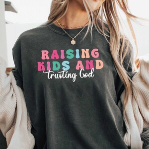 May include: A dark grey t-shirt with the text "Raising Kids and Trusting God" in rainbow colors.