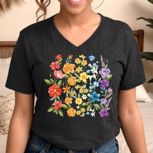 May include: A dark grey V-neck t-shirt with a colorful floral design. The flowers are arranged in a rainbow pattern, with red, orange, yellow, green, blue, indigo, and violet flowers.