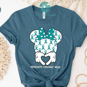 May include: Teal blue t-shirt with a teal and white Mickey Mouse head design. The Mickey Mouse head is covered in teal ribbon designs and the text "STRENGTH-COURAGE-HOPE" is printed below the head.