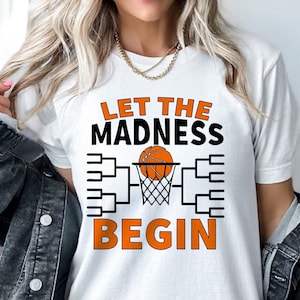 May include: White t-shirt with the text "Let the Madness Begin" and a basketball going through a hoop with a bracket behind it.