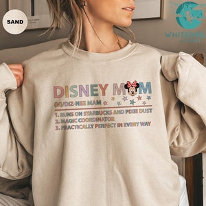 May include: A beige sweatshirt with a colorful graphic that says "Disney Mom" with a Minnie Mouse illustration. The text below the graphic says "(N)/DIZ-NEE MAM" and lists three reasons why a Disney Mom is the best.