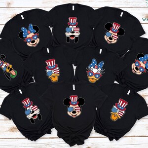 May include: Nine black t-shirts with different Disney characters wearing red, white, and blue patriotic hats and sunglasses. The characters include Mickey Mouse, Minnie Mouse, Donald Duck, Goofy, and Daisy Duck.