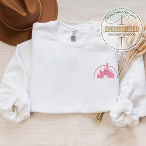 May include: White sweatshirt with a pink embroidered image of a castle on the left chest. The text "Personalized Gift" and "Embroidered Sweatshirt & Hoodie" is on a circle above the sweatshirt.