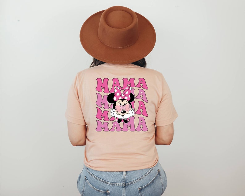 以下が含まれることがあります： 桃色のTシャツに、ピンクとパープルのミニーマウスのグラフィックがプリントされています。"MAMA"という文字が4回繰り返されています。