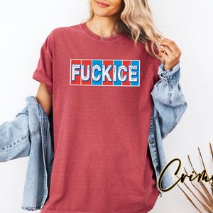 以下が含まれることがあります： 長方形のデザインで「FUCKICE」という文字が入ったマルーン色のTシャツ。テキストは白で、赤と青のアクセントが付いています。シャツはデニムジャケットと合わせて着用されています。
