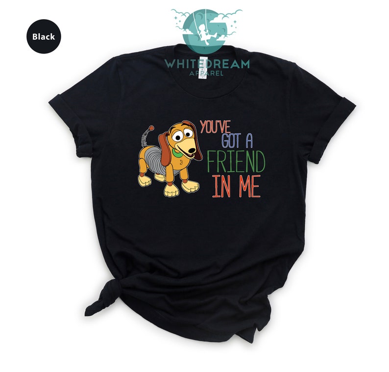 Op de afbeelding: Zwart T-shirt met een cartoon afbeelding van een hondenspeelgoed uit de Toy Story-filmfranchise. De tekst "You've got a friend in me" staat in kleurrijke letters op het shirt gedrukt.