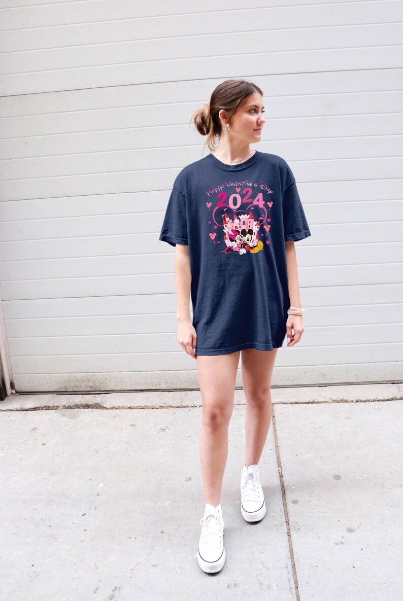 May include: A navy blue t-shirt with a pink graphic of Mickey Mouse and Minnie Mouse in front of a pink castle with the text "Happy Valentine's Day 2024".