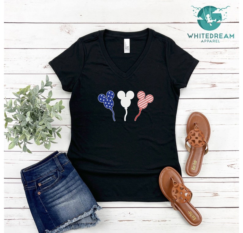 Puede incluir: Camiseta negra de cuello en V con un gr&aacute;fico de tres globos con forma de cabeza de Mickey Mouse. Los globos est&aacute;n decorados con estrellas y rayas rojas, blancas y azules, que se asemejan a la bandera espa&ntilde;ola.